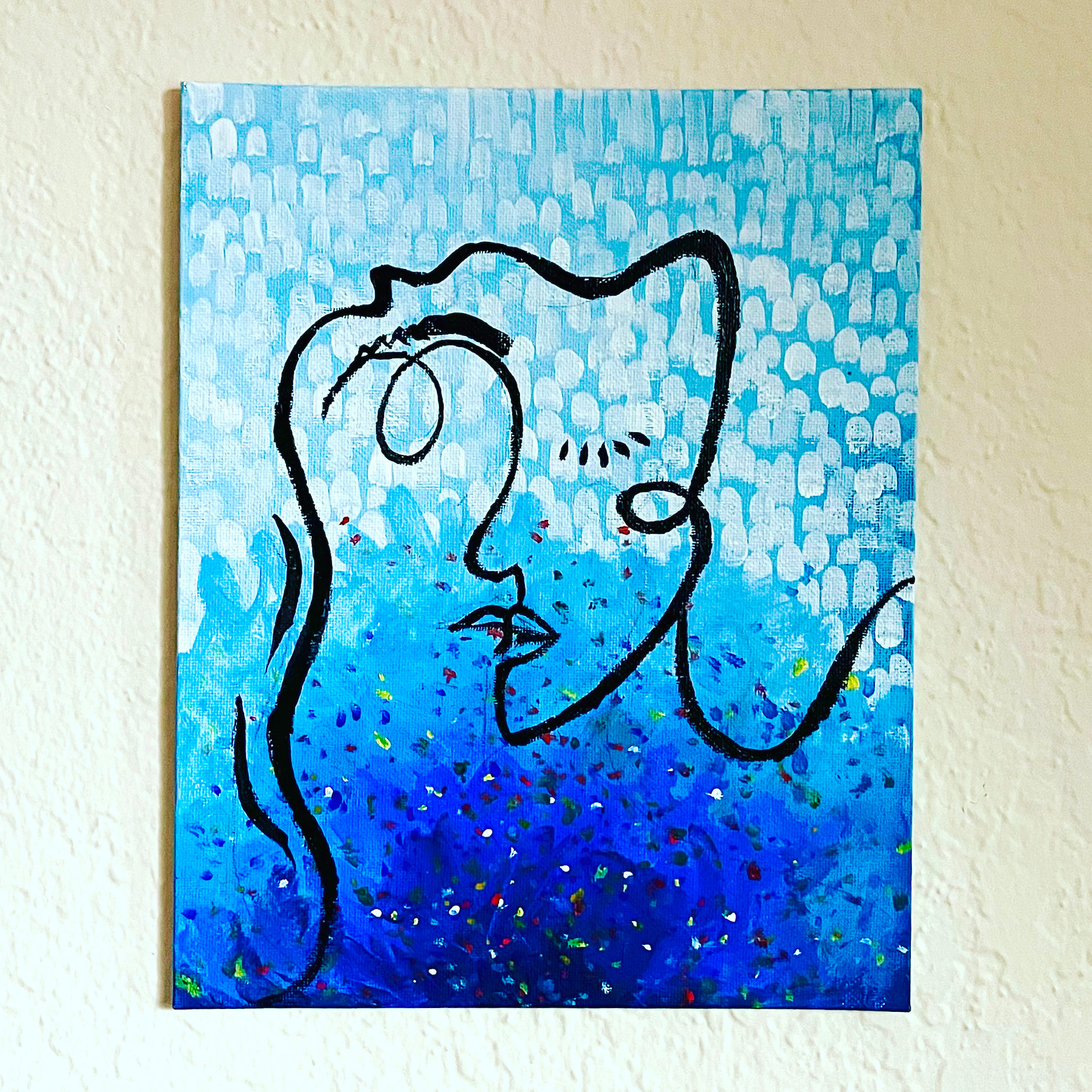 A single continuous black line describes a face in profile on a canvas that fades from pale dotted blue at the top to deep speckled blue below. The canvas hangs on a white textured wall.