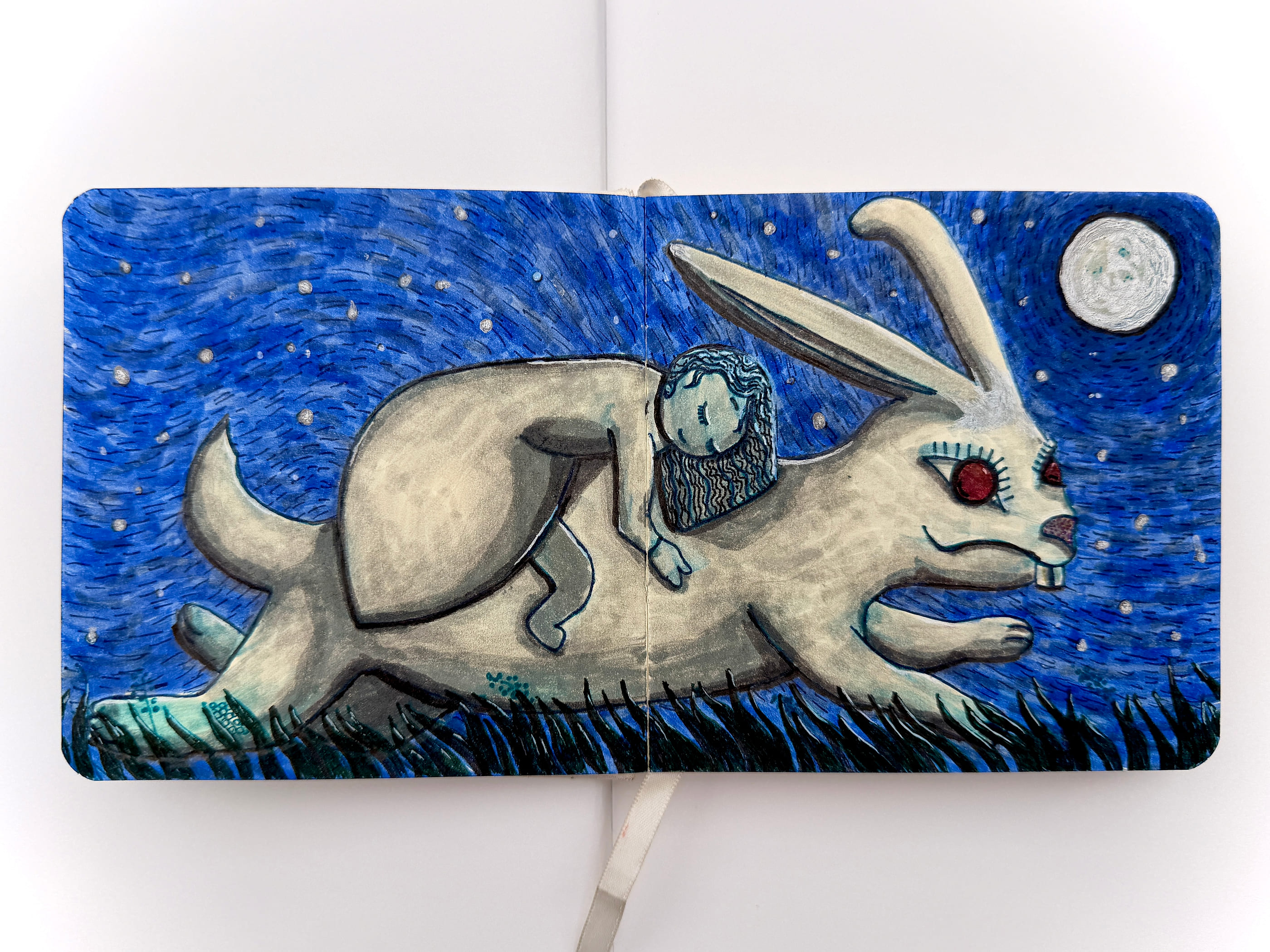 An open sketchbook spread showing a large pale hare leaping across black grass beneath a deep blue night sky worked in swirling strokes, scattered with white stars and a full moon. A small dark-haired girl lies stretched along the hare's back, holding on, and the hare's eye is a bright red circle.