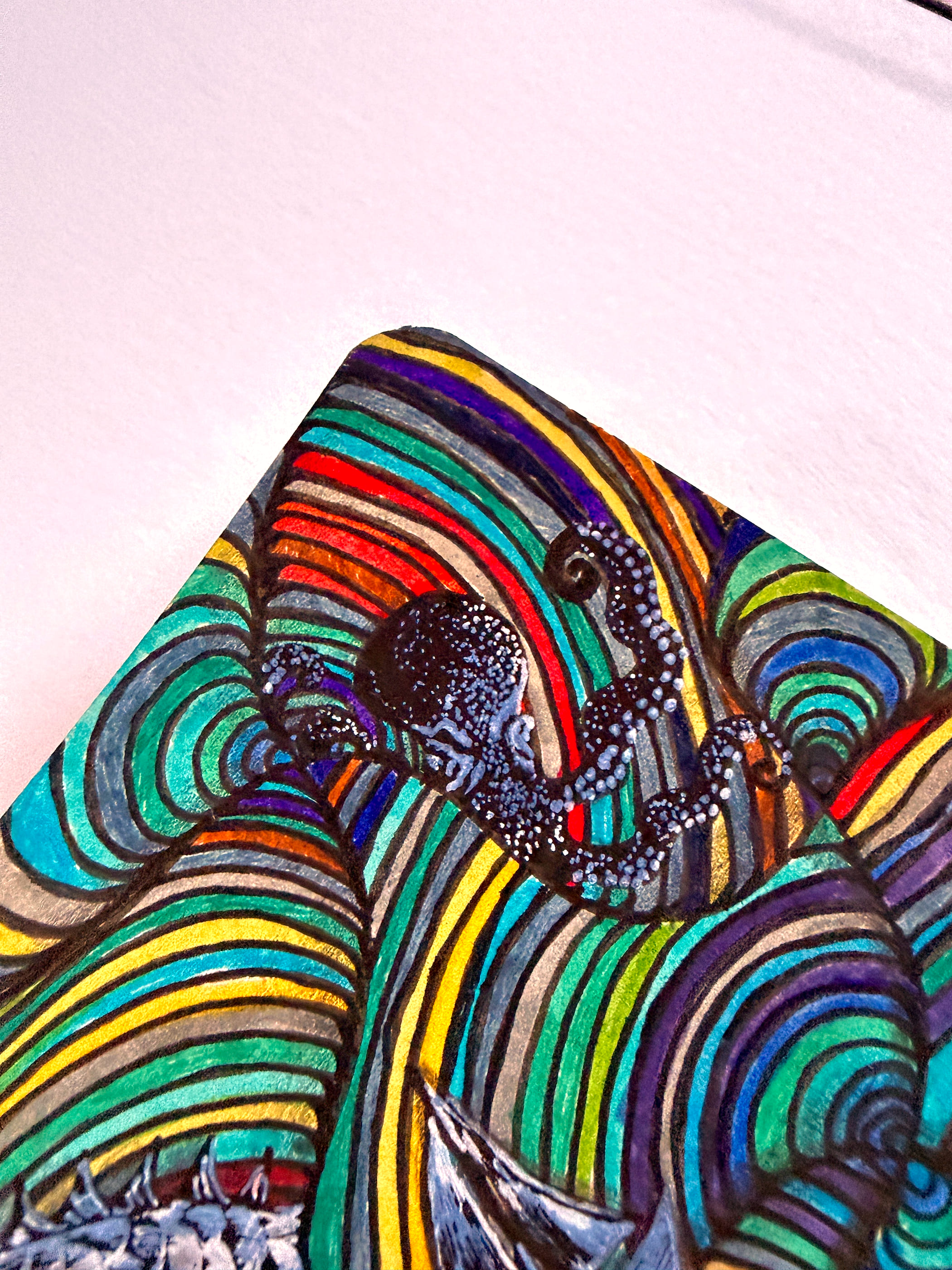 A close view of one corner of the spread, lit from the side so the marker strokes catch the light. A dark octopus with pale dotted tentacles curls through banded waves of red, yellow, teal and violet.